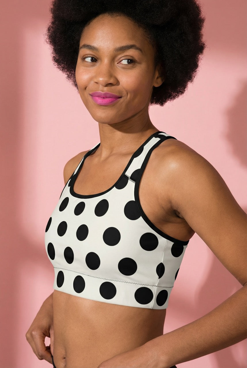 Woman wearing a black and white polka dot sports bra against a pink background
