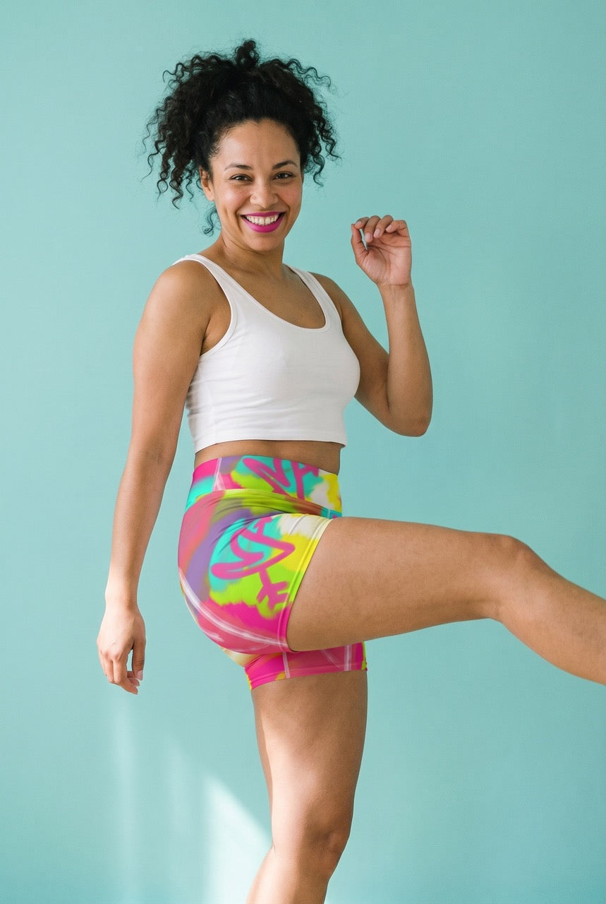 Woman wearing a white sports bra and colorful bike shorts against a light blue background
