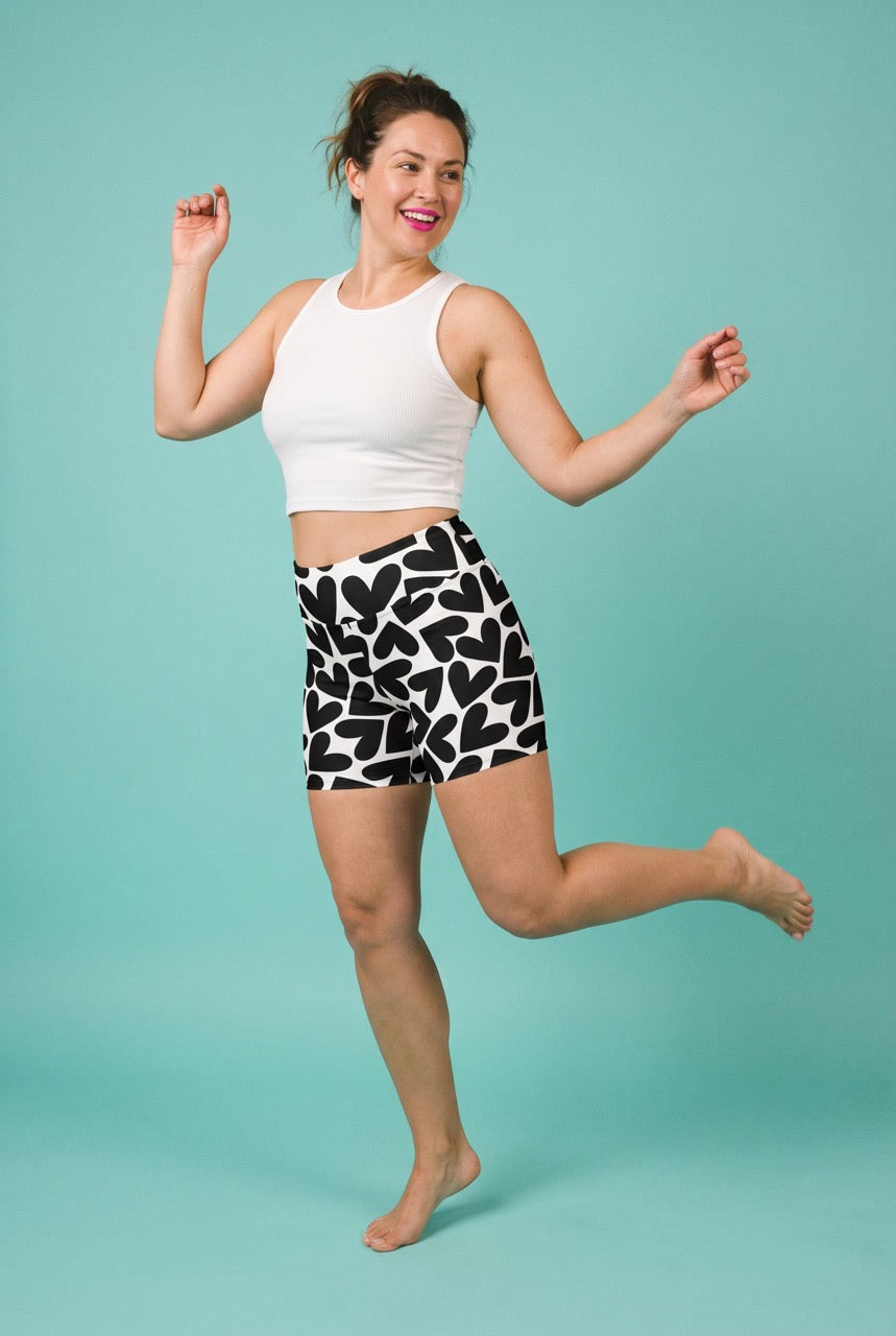 Woman wearing a white crop top and black and white patterned shorts on a teal background