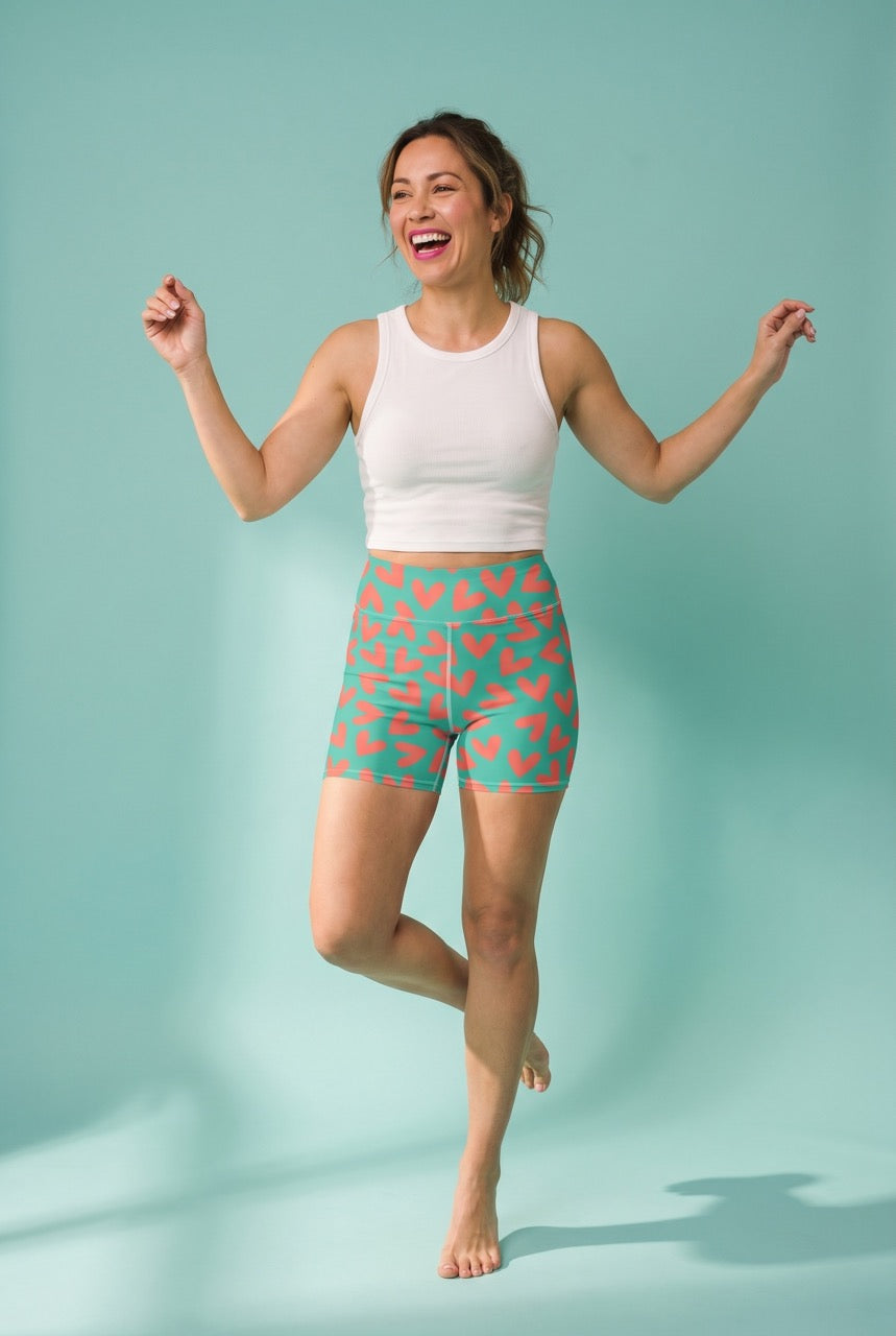 Woman wearing a white tank top and green heart-patterned shorts on a light blue background