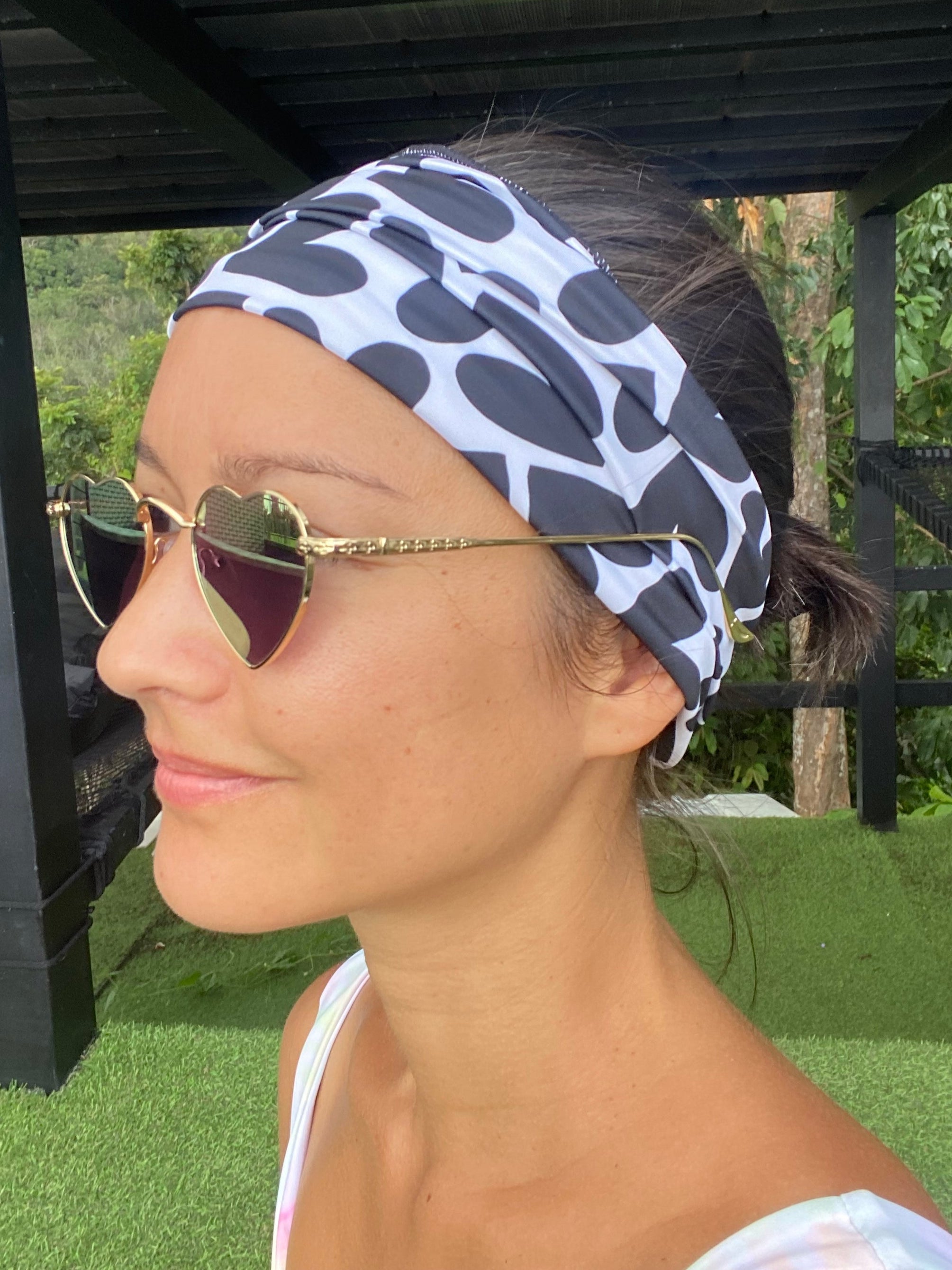 Person wearing a black and white hearts headband with sunglasses on a green outdoor background