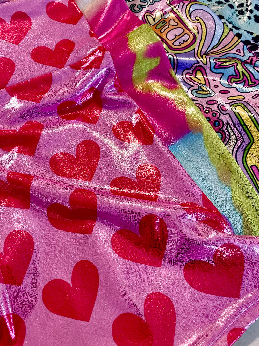 Pink glitter shorts with red heart patterns and colorful glitter fabric in the background.